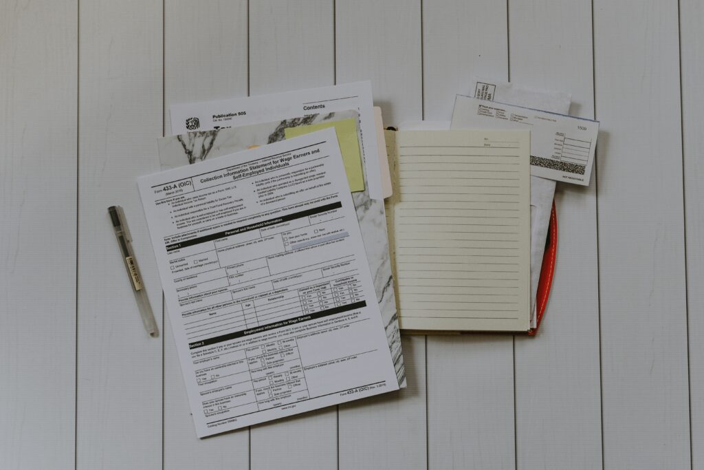 A stack of tax documents alongside a pen and notebook—all set to research tax filing options.