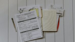 A stack of tax documents alongside a pen and notebook—all set to research tax filing options.