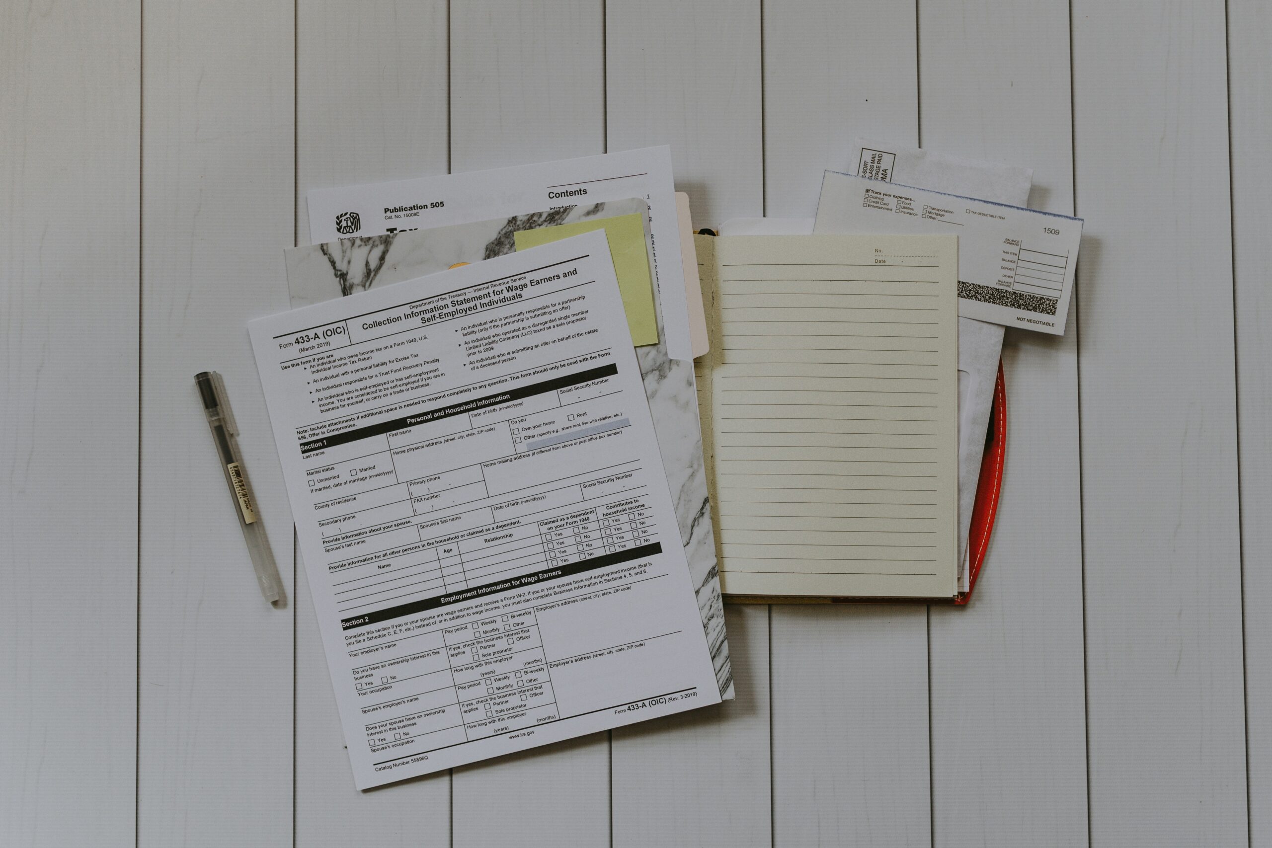 A stack of tax documents alongside a pen and notebook—all set to research tax filing options.