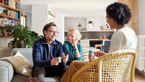 Cheerful adult couple in casual clothes having meeting with tax advisor in living room at home during daytime