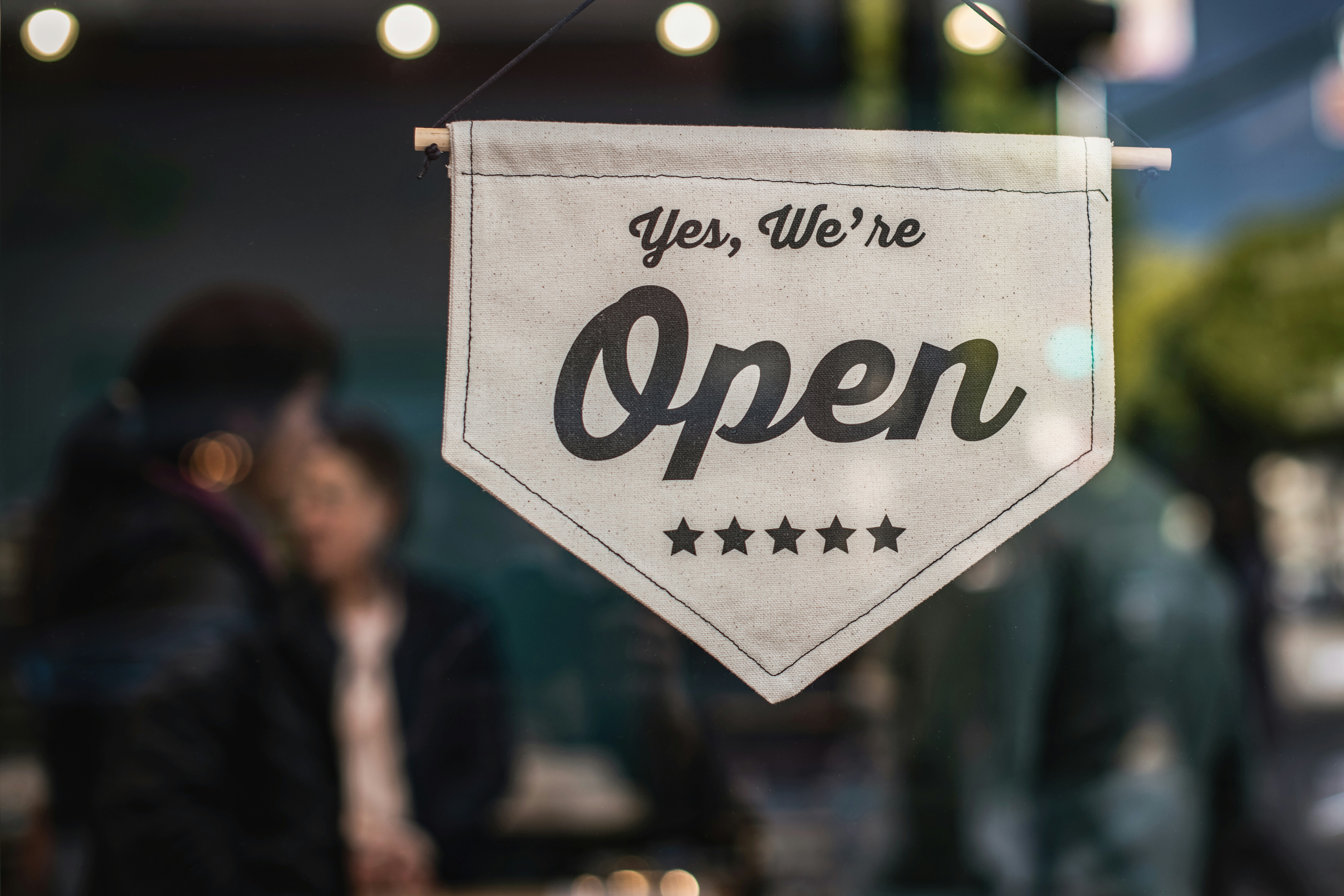 A cream colored sign on a blurry background that says "Yes, We're Open."