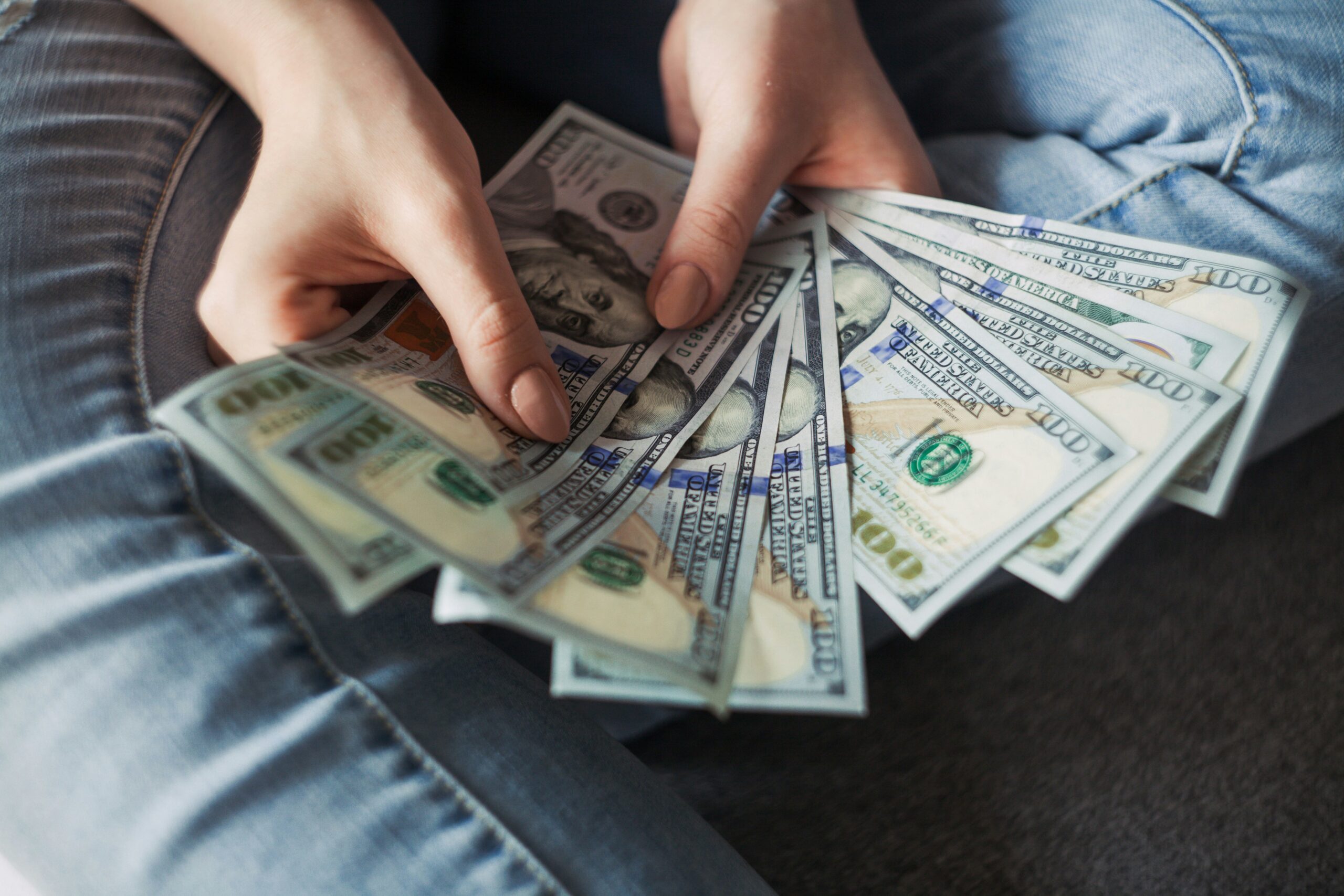 A hand fans out several $100 bills, representing high levels of passive income that may be subject to the Net Investment Income Tax (NIIT). The image reflects the importance of tax strategies to help investors protect more of what they earn.