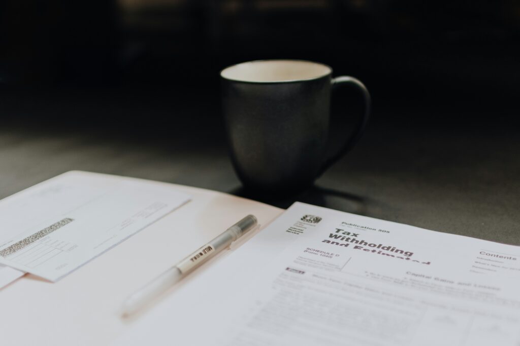 A coffee mug sits next to an open folder containing a tax withholding document, illustrating the paperwork involved in completing a W-4 form accurately and managing paycheck withholdings.