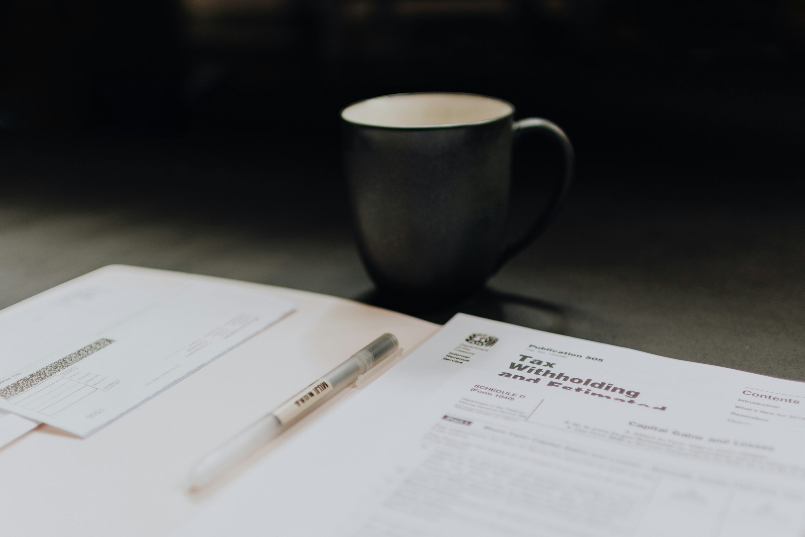 A coffee mug sits next to an open folder containing a tax withholding document, illustrating the paperwork involved in completing a W-4 form accurately and managing paycheck withholdings.