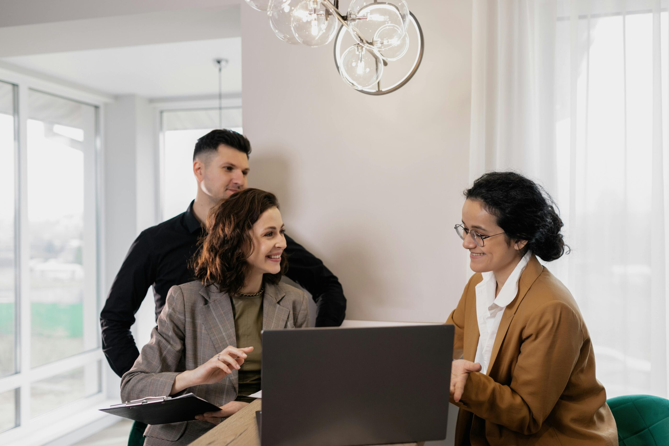 Two real estate investors meet with a financial advisor to discuss tax strategies for property investments, seated together with a laptop in a modern office.