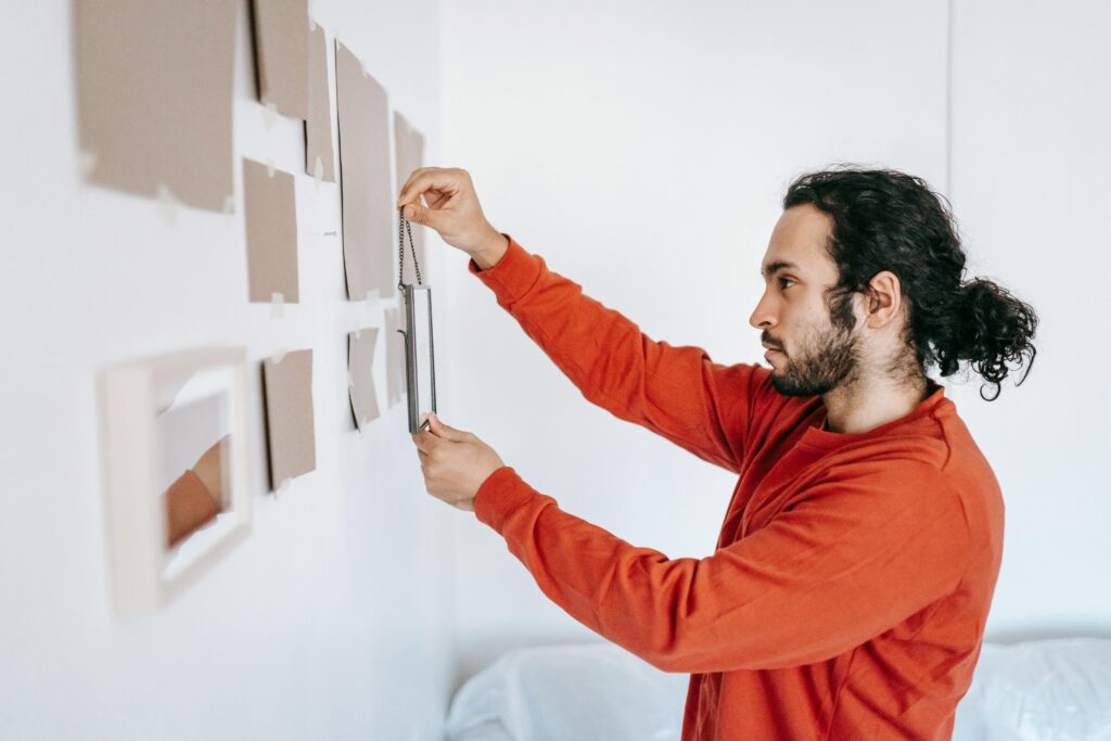 A man in a modern, minimalist living room carefully hangs a framed picture on the wall—symbolizing the thoughtful financial planning high net worth individuals must undertake in response to the "One Big Beautiful Bill." Just as placing a single frame can redefine a space, this sweeping tax legislation could reshape estate strategies, investment decisions, and long-term financial legacies.