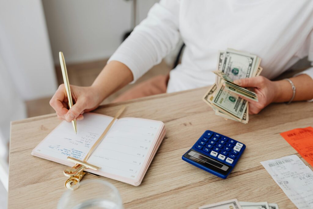 An image of someone writing in a notebook whilst holding money. Sitting up at a table.