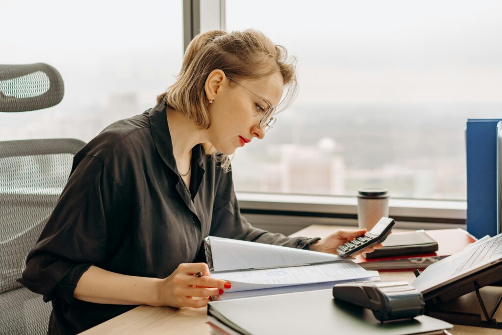 A tax professional uses a calculator and computer to manually complete paperwork—illustrating the time-intensive tasks that AI-powered automation can now streamline.