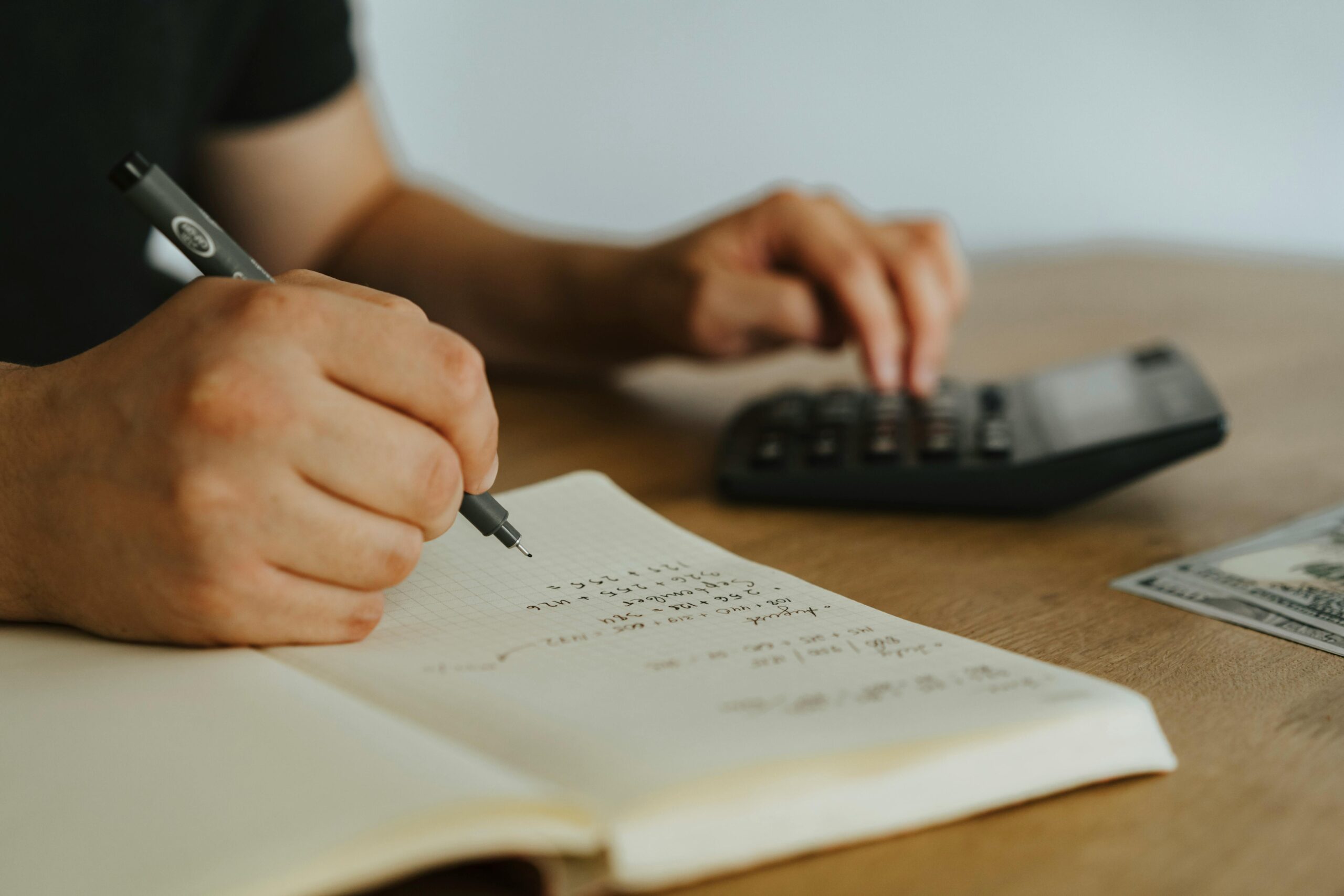 Person calculating taxes with notepad and calculator.