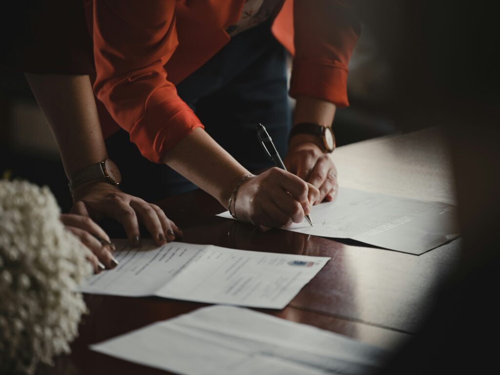 A person in an orange shirt fills out a paper form with a pen, symbolizing the step-by-step process of completing a W-4 to ensure proper tax withholding.