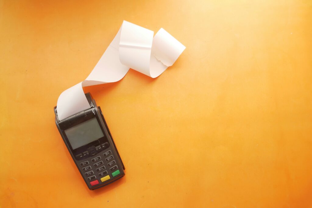 A smartphone beside a roll of printed receipts on a wooden table, emphasizing the importance of maintaining accurate documentation while working remotely—crucial for managing budgets, reimbursements, and remote work tax deductions.