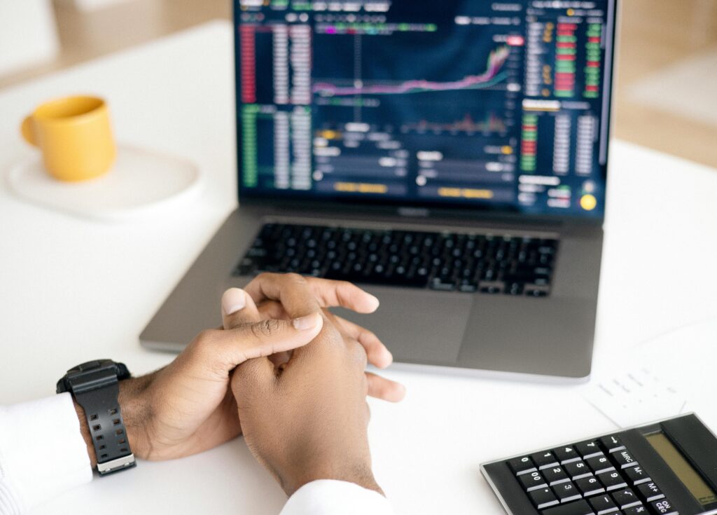 A person sits at a desk with hands clasped, facing a laptop displaying colorful stock market charts and data, alongside a calculator—illustrating the analysis and strategic planning involved in ESG investing to potentially enhance returns and leverage tax-saving opportunities.