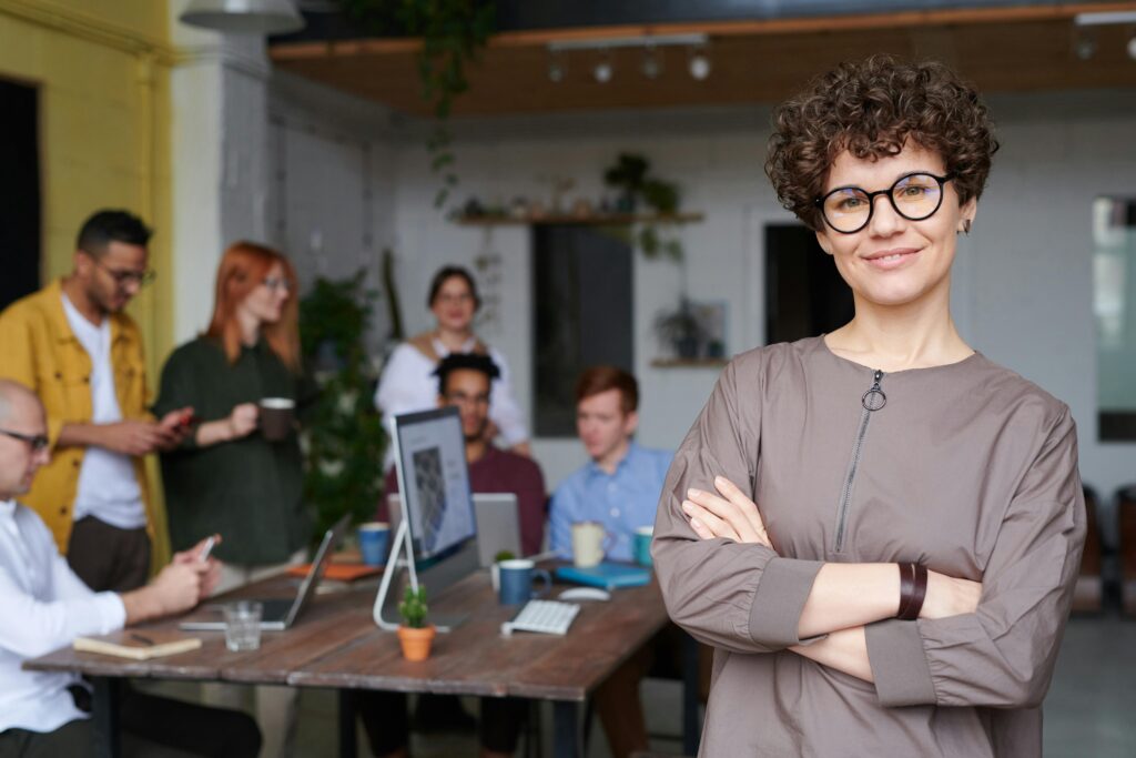 Entrepreneur standing aside from her team at work around a conference table. Business owners everywhere stand to gain big from Trump's signature legislation, "One, Big, Beautiful Bill" (OBBB).