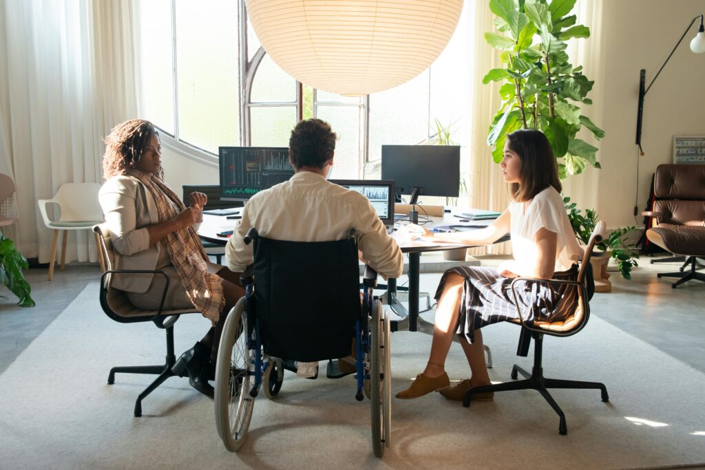 A group of coworkers holding a meeting with external monitors and stacks of tax documents to be filed.