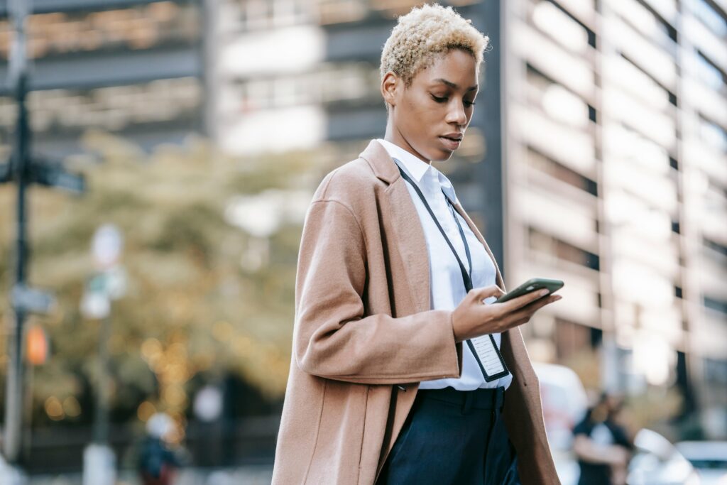 A focused businesswoman stands on an urban street, intently browsing her smartphone—capturing the vigilance entrepreneurs must maintain as they navigate the evolving tax landscape under the "One Big Beautiful Bill." With potential changes to capital gains, entity structures, and deductions, staying informed is essential to protecting and growing a business.