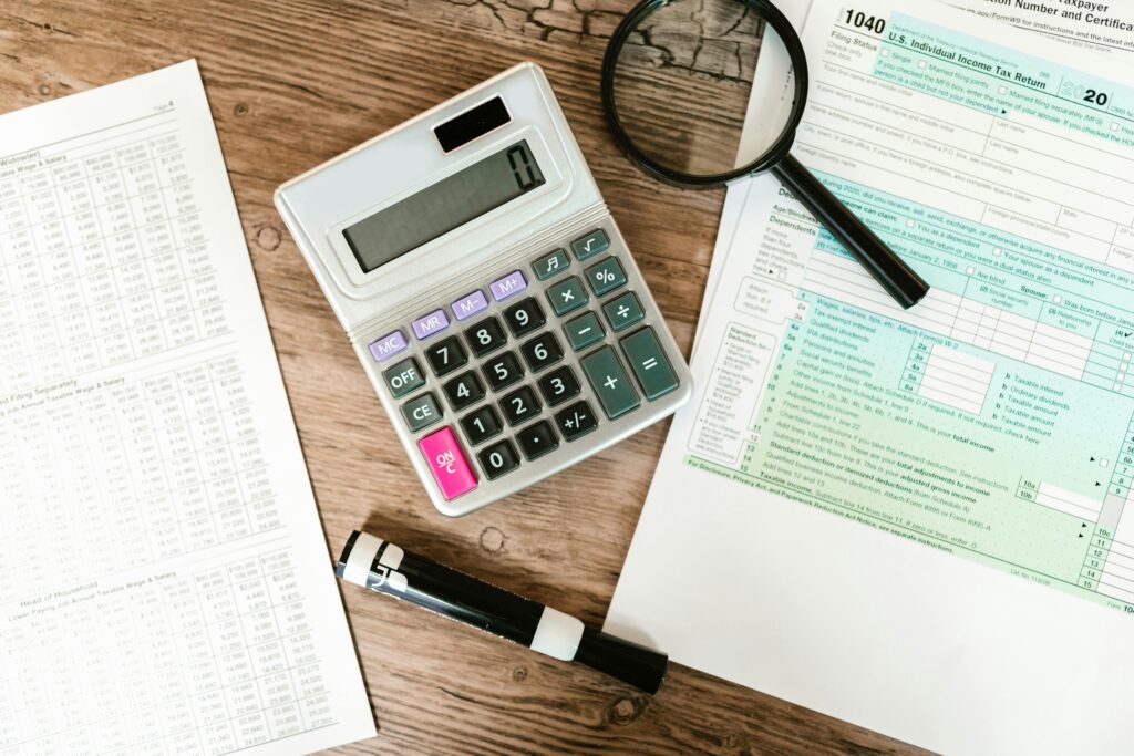 A calculator and magnifying glass placed over tax documents—highlighting the detailed review process required when calculating and reporting cryptocurrency gains on your tax return.