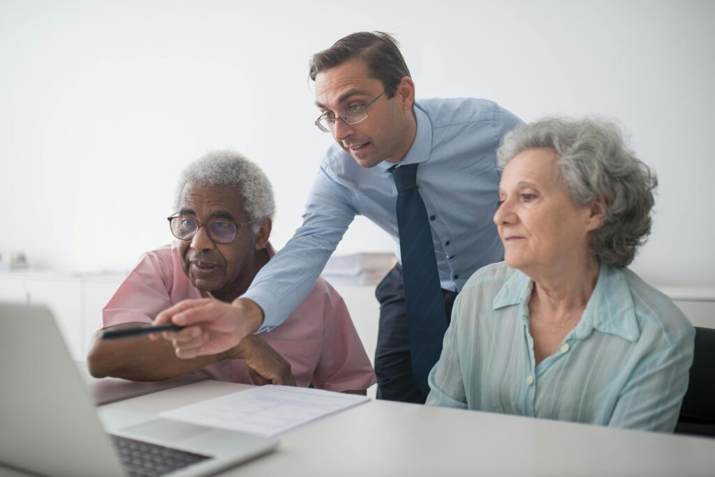A financial advisor points to a laptop screen while explaining information to two elderly clients, symbolizing how adjusting entries help present a clear and accurate picture of a company’s finances to stakeholders.
