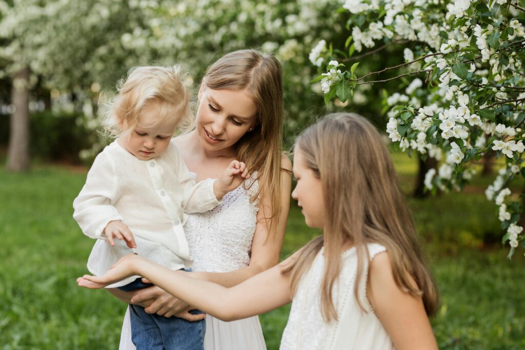A mother holds a toddler while an older child interacts with them in a blooming garden, reflecting the long-term family benefits of superfunding a 529 plan for multiple children.