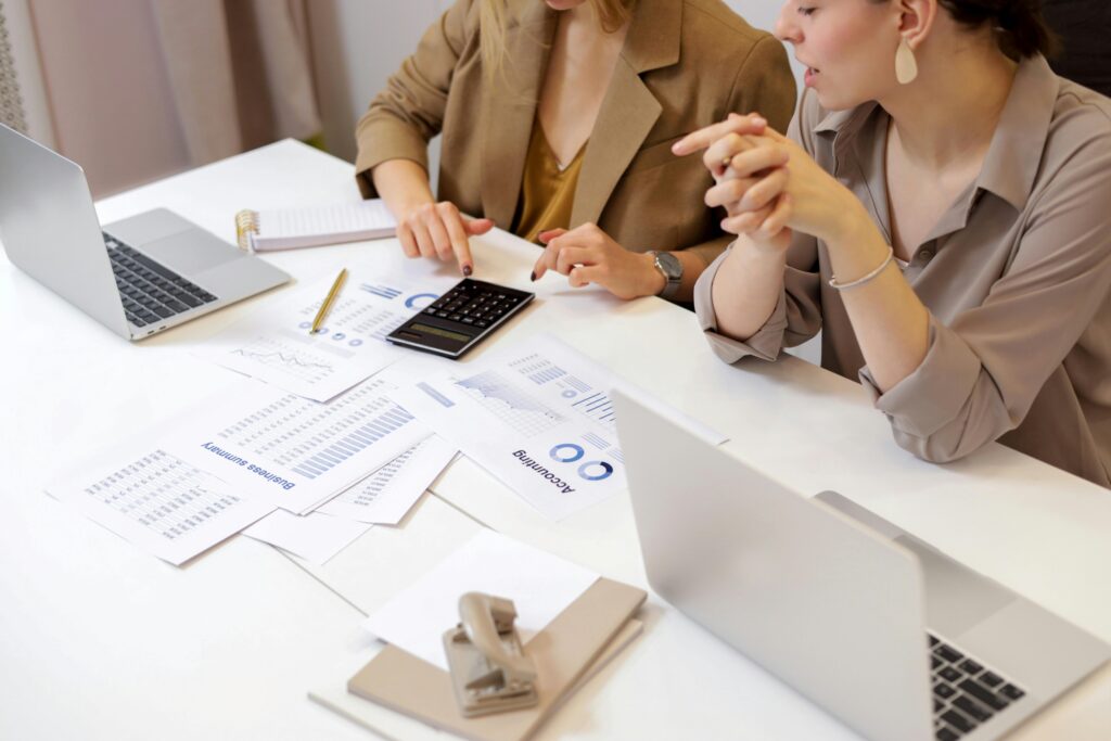 Two colleagues analyze printed financial reports and data charts with a calculator, representing collaboration in preparing adjusting entries that align revenue and expenses correctly.