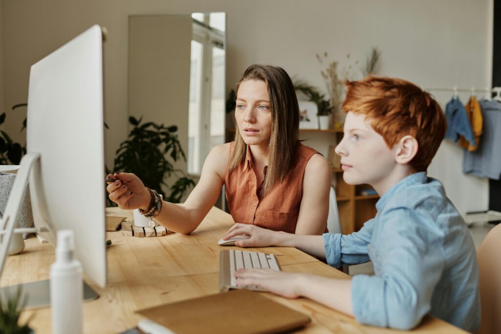 A woman points to a computer screen while guiding a young boy, symbolizing proactive financial planning for a child’s educational expenses through a 529 plan.