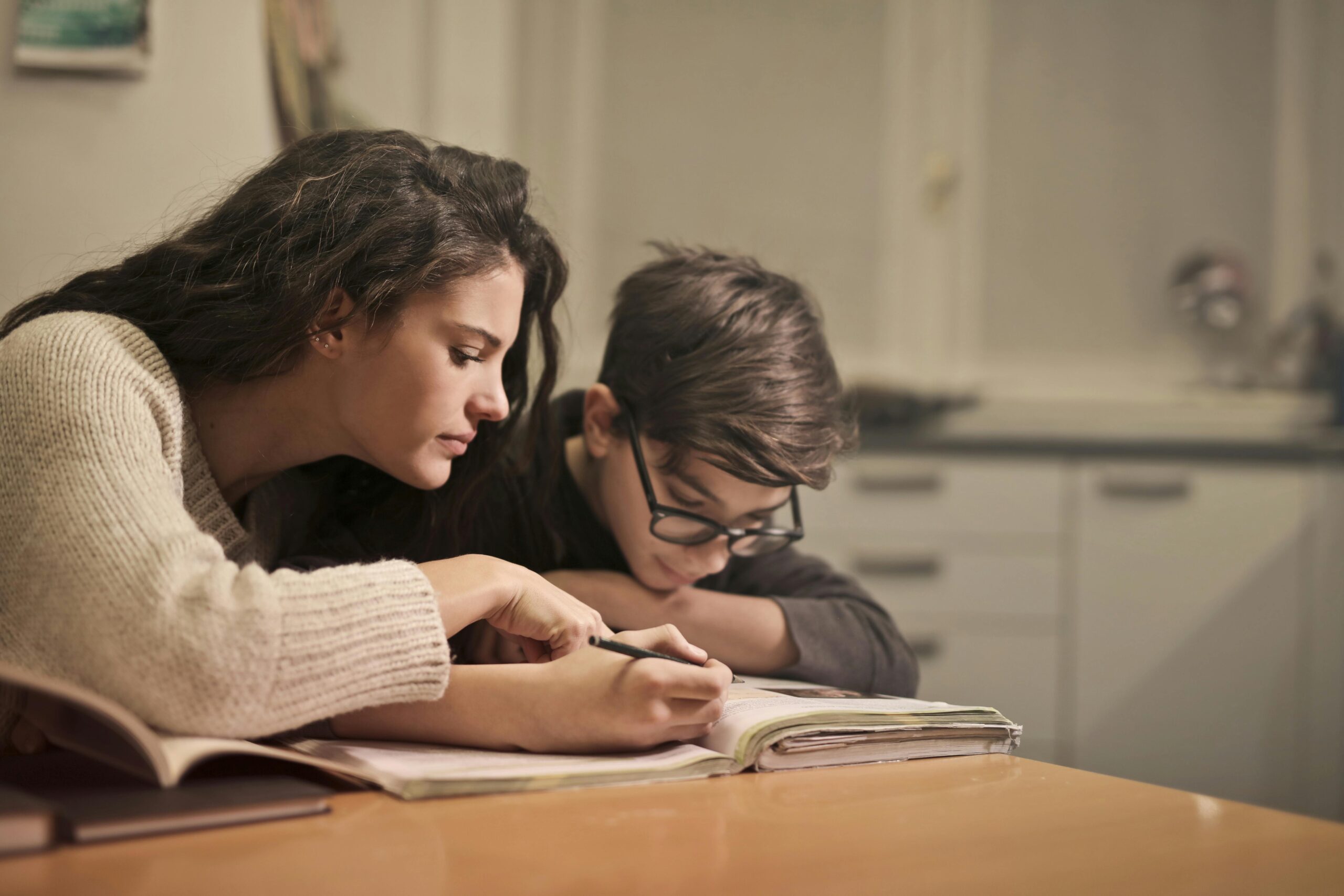 A mother leans over to help her young son with homework at the kitchen table, representing how 529 plan savings can support a child’s future education.