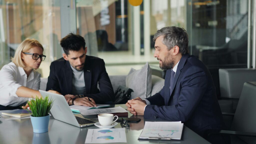 Three business professionals collaborating at a table with laptops, illustrating the importance of teamwork and resource sharing for tax advisors.