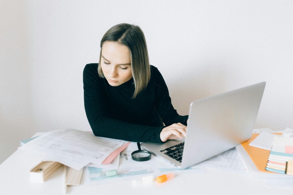 One Big Beautiful Bill: a woman in black long sleeves doing paperwork while typing on her laptop.